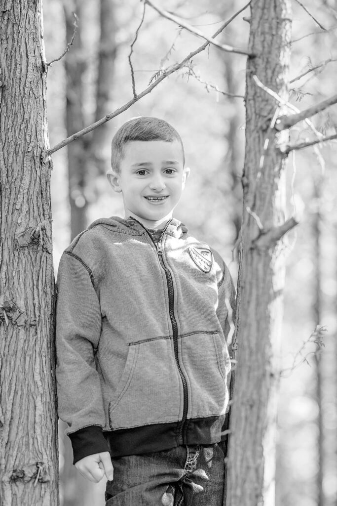 A black and white photo of a young boy standing in a tree, smiling at the camera.