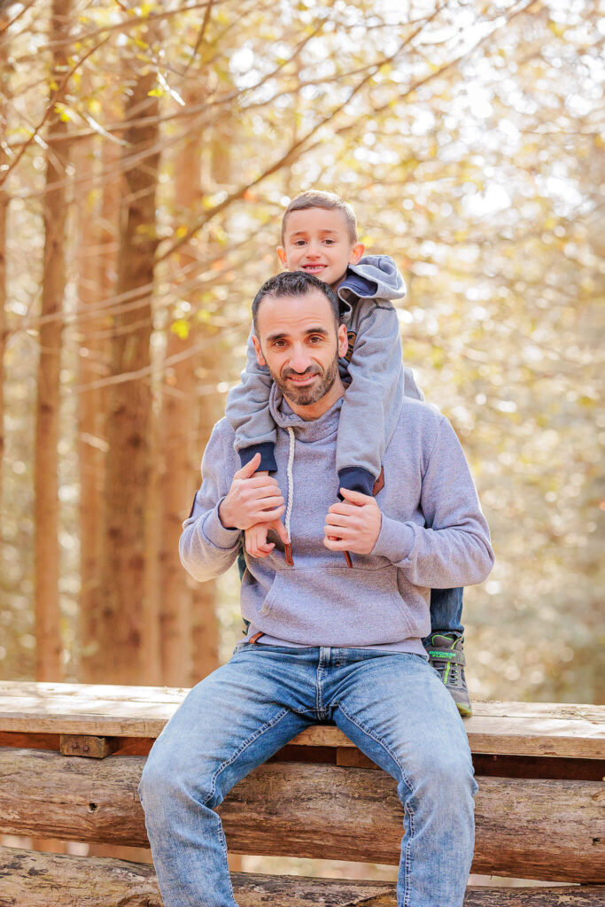 A young boy on his father's back, looking and smiling at the camera.