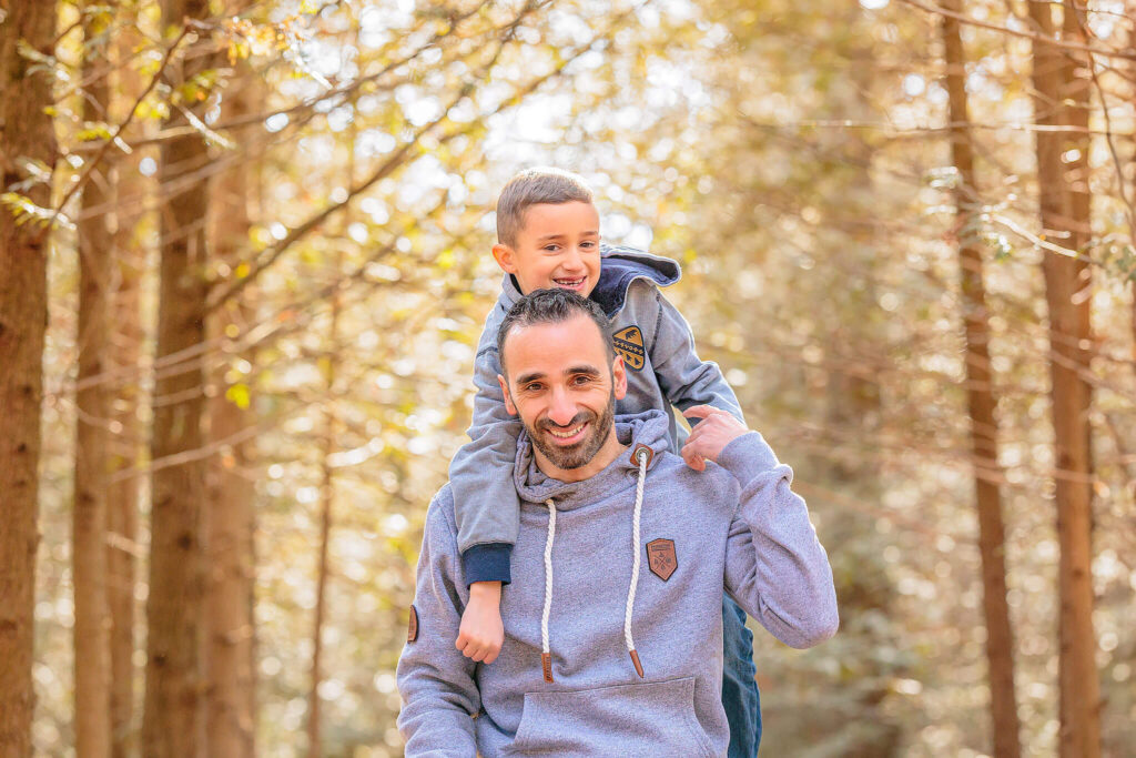 A young boy on his father's back, looking and smiling at the camera.