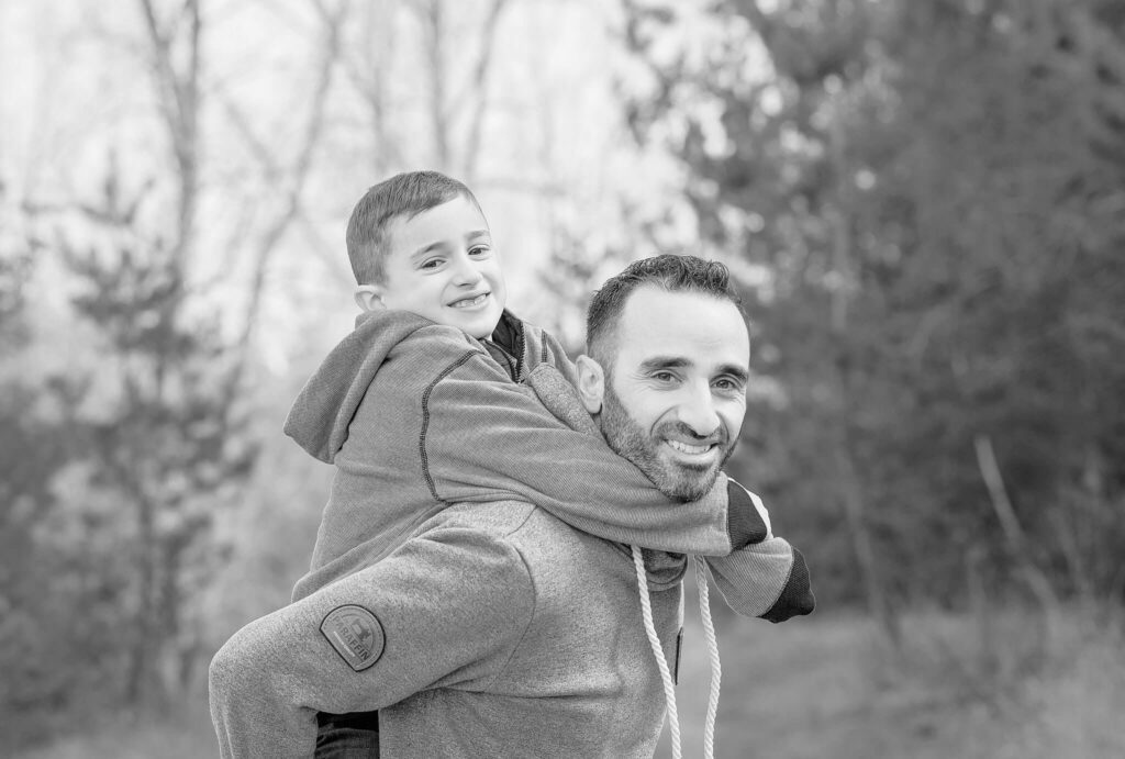 A young boy on his father's back, looking and smiling at the camera.