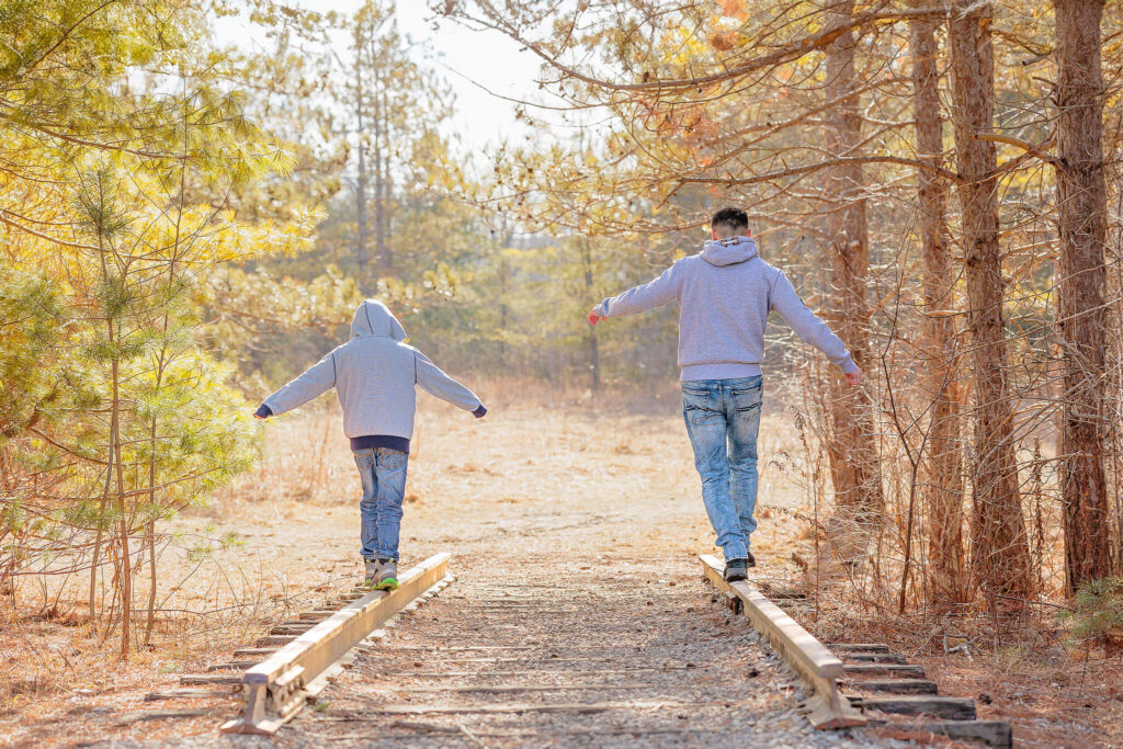 A young boy and his dad balancing on old, no longer being used, railroad tracks