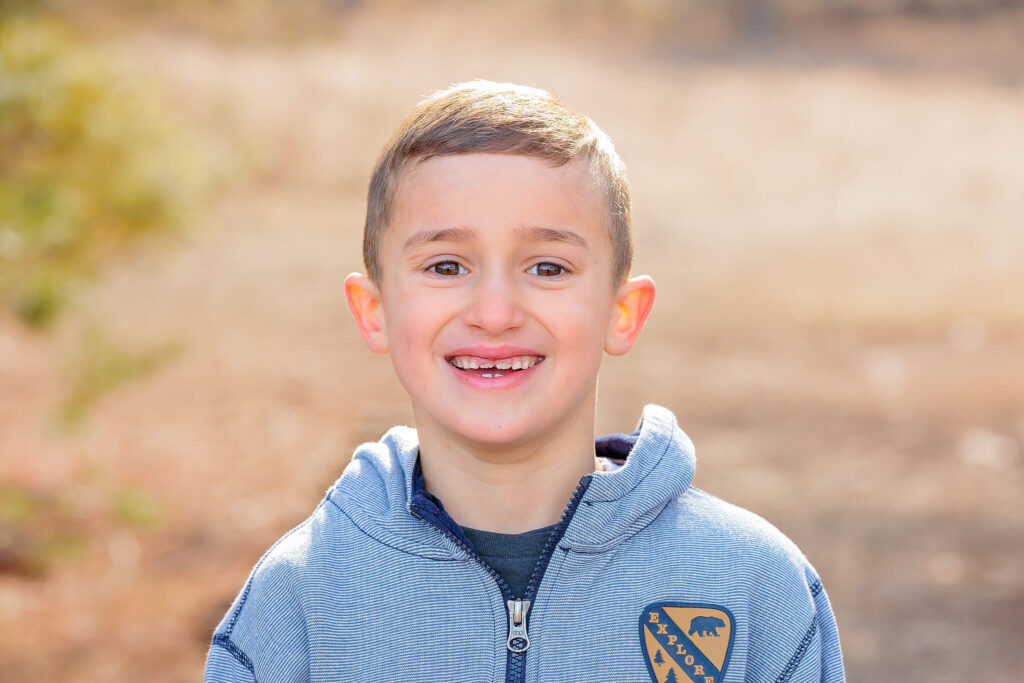 A close up portrait of a young boy smiling happily at the camera during a photo session.