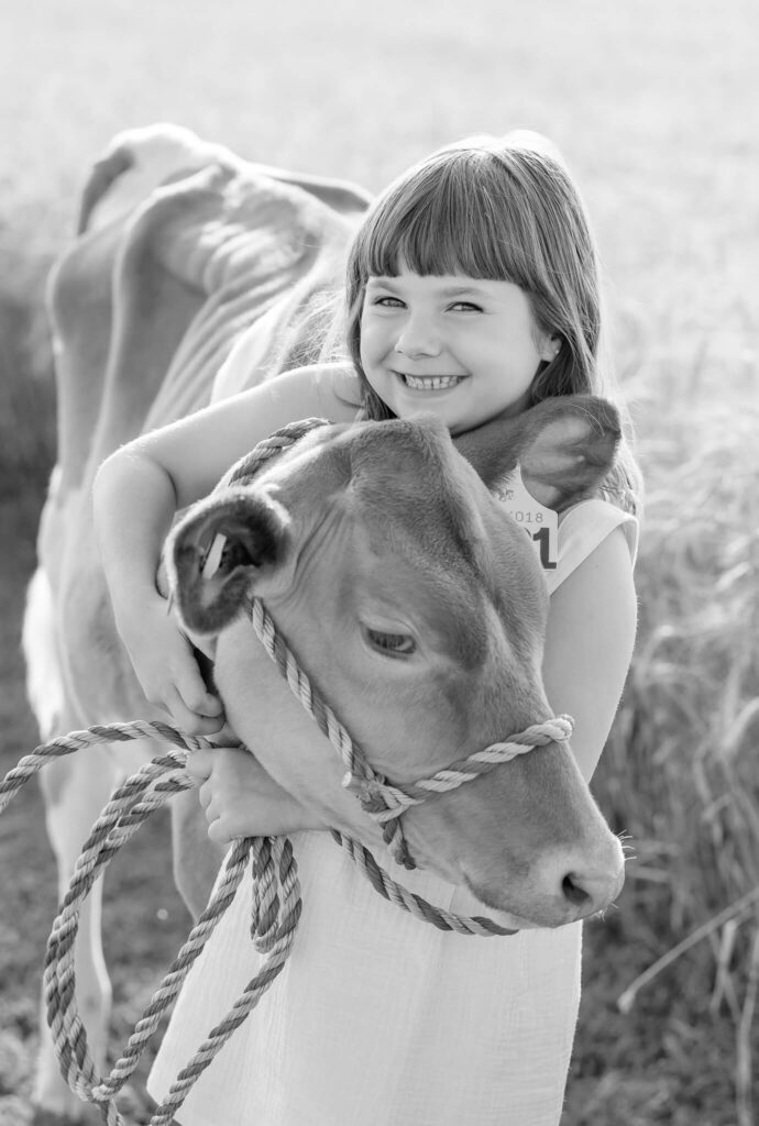 Black and white portrait of a smiling girl embracing her beloved 4H dairy calf.