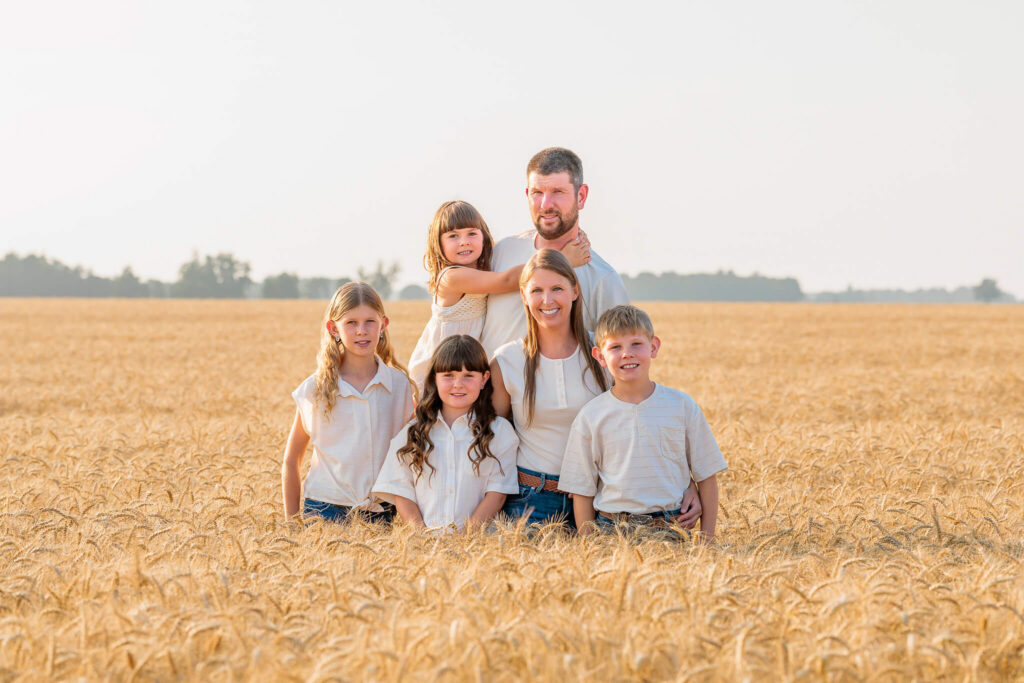 Parents and four children standing together in a golden wheat field during an outdoor family session.