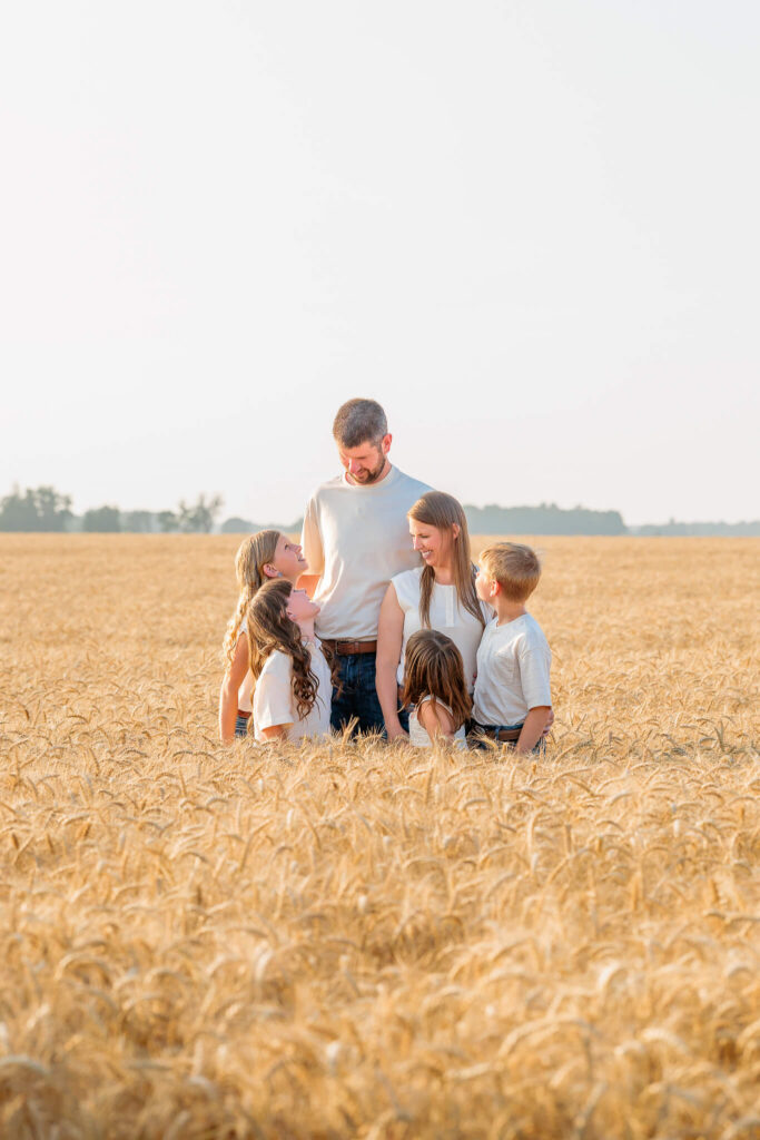 Parents and four children smiling together in a golden wheat field during an outdoor family session.