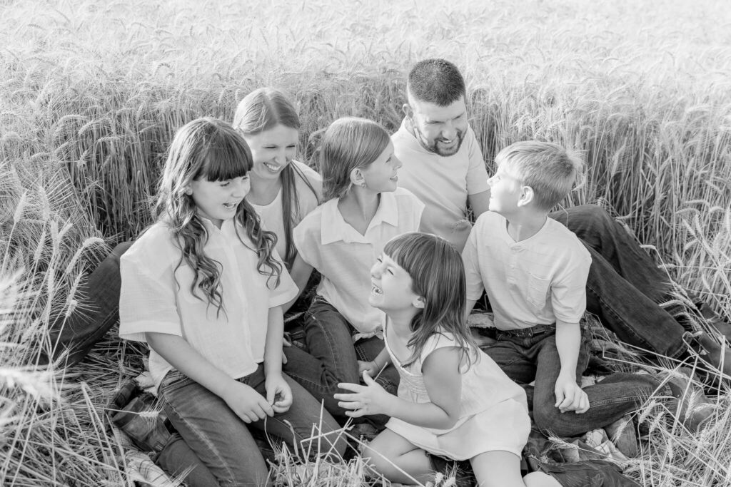 Black and white photo of family laughing together in a wheat field.
