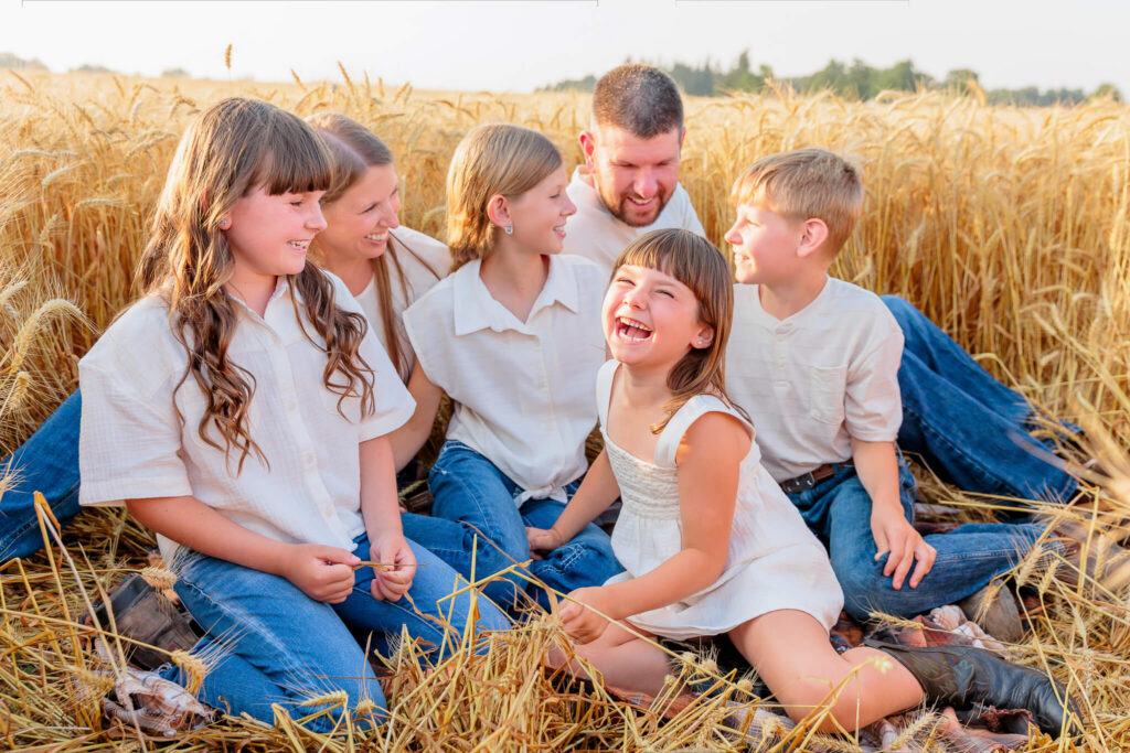 Candid colour photo of family of 5 laughing together in a wheat field during a photo session in Thamesford, Ontairo.