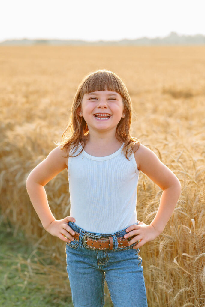 Smiling young girl standing confidently in front of a golden wheat field.