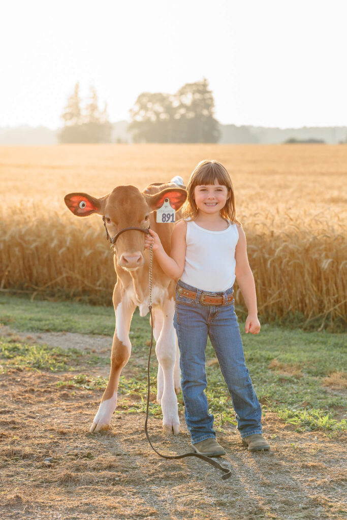 Young girl standing proudly beside her dairy calf on the family farm in Thamesford, Ontario.